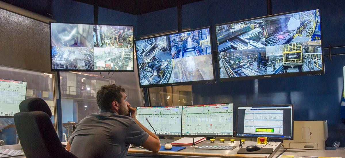 A relaxed operator sits in the central operation cockpit of a Hot Strip Mill pulpit, comfortably monitoring and controlling the entire mill through advanced control panels and screens.
