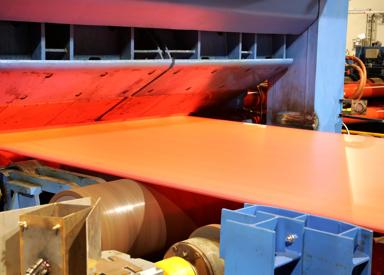Hot steel strip exiting the roll gap with excellent contour and flatness, controlled by the Contour and Flatness Optimizer system that uses advanced algorithms and online material flow modeling to enhance steel strip quality and production efficiency.