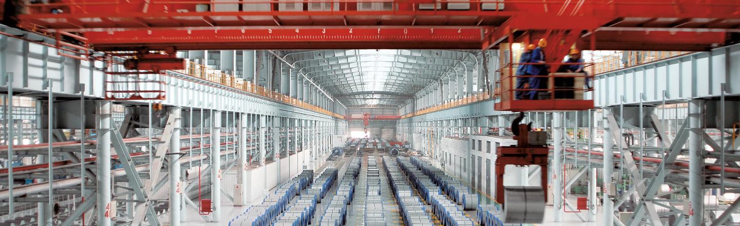 Overhead crane operating in steel plant with rows of coils, illustrating structural monitoring environment for industrial operations
