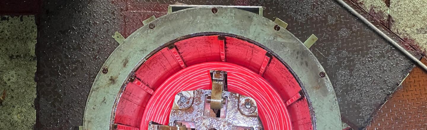 Overhead view of a top‑down pouring reel forming a glowing red bar‑in‑coil at a wire rod and bar‑in‑coil mill