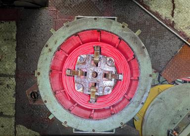 Overhead view of a top‑down pouring reel forming a glowing red bar‑in‑coil at a wire rod and bar‑in‑coil mill