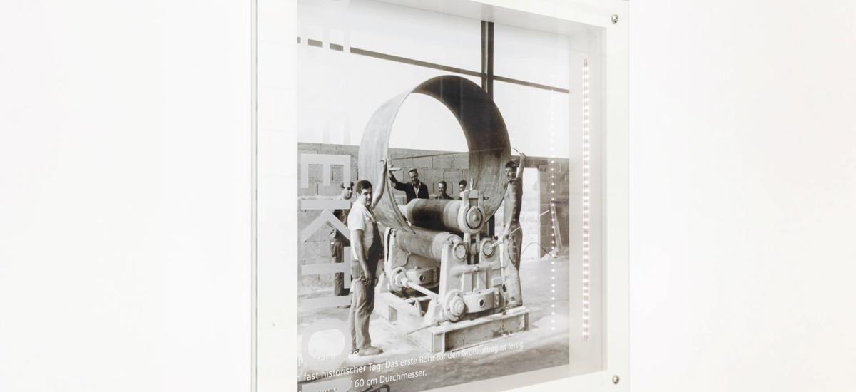 Placed along the open stairway are reminders of the legacy of Fuchs Systemtechnik. Among them are photos from 1969, including an advertisement and presentation of  the completion of a 160-centimeter- diameter pipe. Proud of their legacy and with the original manufacturing building just a little over 100 meters away, colleagues at Legelshurst  often reflect on past innovations  and successes, when preparing for  the future.